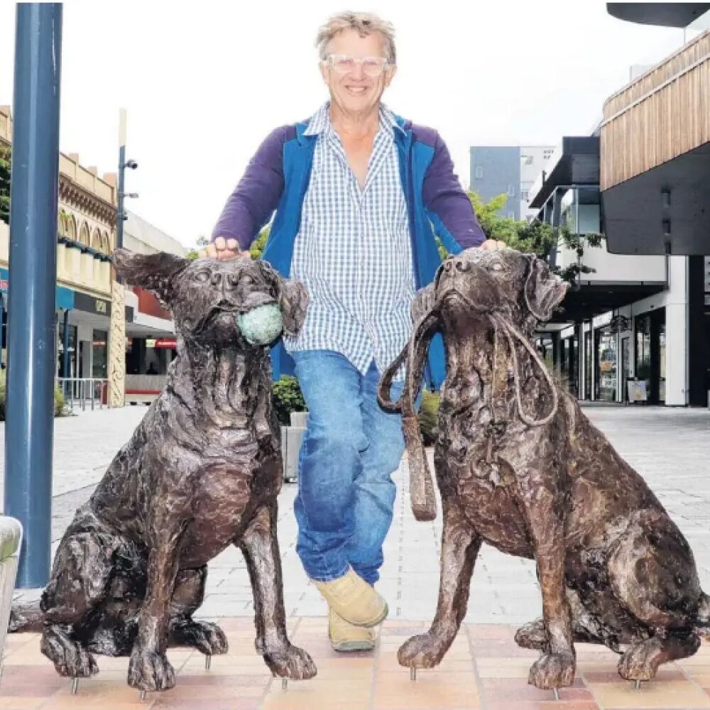 Richard Wells, stands beside his large two Lab­rador bronze sculptures — one with a ball in its mouth, the other with a leash, ready for a walk